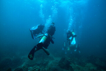Fototapeta na wymiar Scuba Divers, silhouettes against sunburst, in the ocean beside coral reef