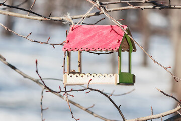 A homemade wooden bird feeder hangs on a spring branch of a tree.