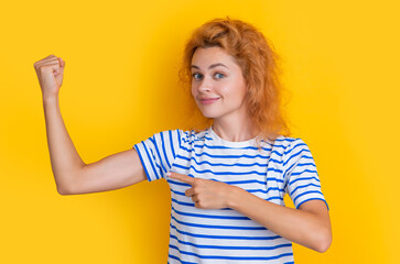 redhead woman show biceps isolated on yellow background. portrait of young redhead woman