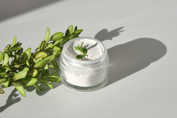 An open jar of facial scrub powder with a green sprig.
