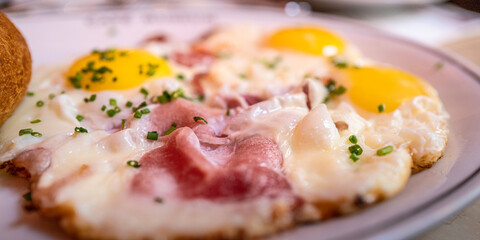Bacon and eggs, sunny side up, with a bread served on a white plate, Austrian style, diagonal close-up view