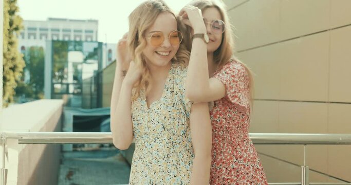 Two young beautiful smiling hipster girls in trendy summer sundress. Carefree women posing on street background 
