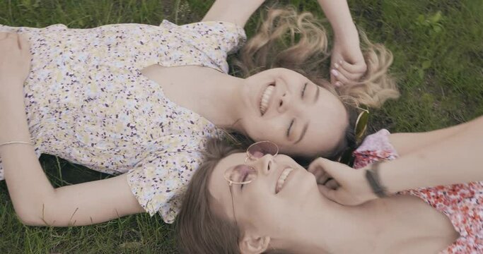 Two young beautiful smiling hipster girls in trendy summer sundress. Sexy carefree women lying on the green grass