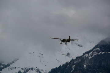 Fototapeta na wymiar Swiss army Pilatus Porter airplane after take off in cloudy and snow covered mountains - bringing paratroopers to high jumping altitude