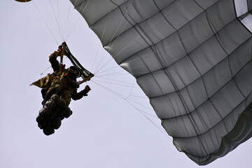 Close-up of Swiss army paratrooper approaching landing in full gear - with grey parachute