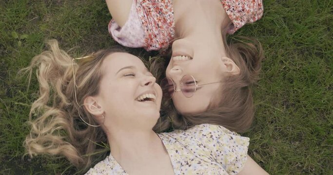 Two young beautiful smiling hipster girls in trendy summer sundress. Sexy carefree women lying on the green grass