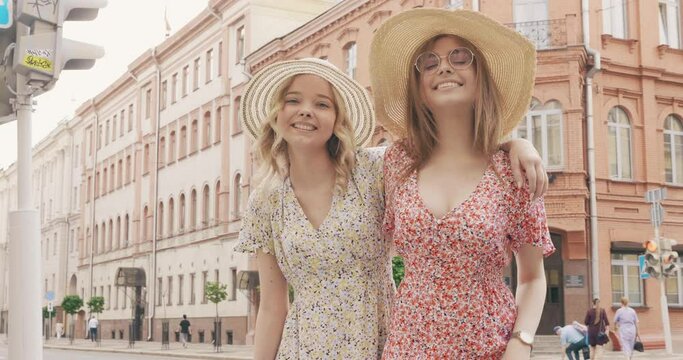 Two young beautiful smiling hipster girls in trendy summer sundress. Carefree women posing on street background in hats at warm sunny day