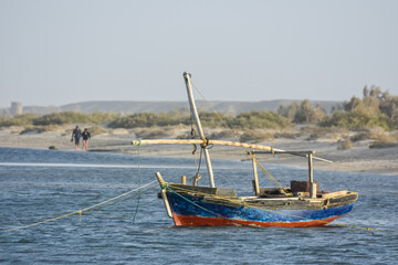 Obraz premium blue and red wooden fisher boat in the sea with two rambler at the beach