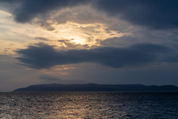This is a landscape of a summer yellow-orange sunset with dark clouds on the beach. The sea, on the horizon the outlines of the mountains Can be used as a background for a calendar, poster