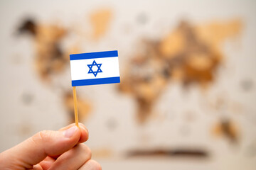 Israel flag in mans hand on the wooden world map background. Global economy and geopolitics...