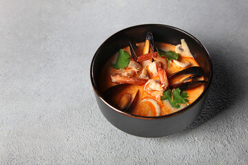 Spicy Thai Tom yam soup with shrimp and mussels in a black bowl. Light background. Copy space.