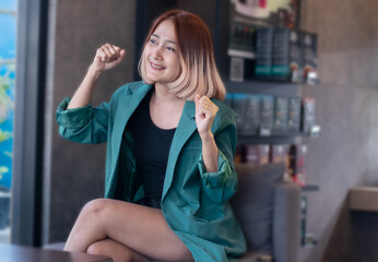 Asian woman wearing a suit green sitting on a sofa inside the cafe and happy dancing smiling having moving, and listening to music, feeling relaxing to enjoy life concepts.