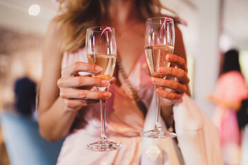 Woman in pink dress holding two glasses of champagne in the hands.