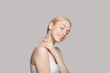 Obraz premium Cute woman with blonde ponytail smiling isolated on grey background. Beauty,cosmetics, skincare, glamour.