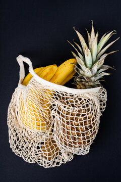 bananas, kiwi and pineapple in a beige string bag on black background