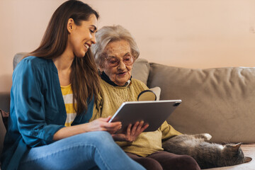 Nurse in a medical visit to an elderly woman, teaching her how to use a digital tablet.