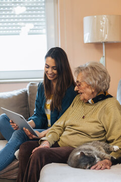 Young woman visiting her grandmother, showing her pictures on digital tablet.