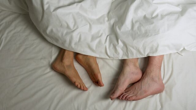  Female and male legs in a white bed under blanket