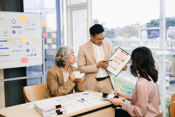 Group of young Asian business people discussing business plan at modern startup in creative business discussing work office building.