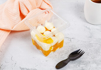 Dessert of cream, jam and orange in a plastic glass on a concrete background.