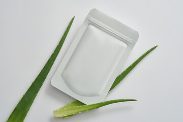 Minimal style for advertising cosmetics - mockup of a facial sheet mask package and aloe vera leaves on white background. Aloe vera has anti-aging effects, prevents wrinkles and stimulates collagen.