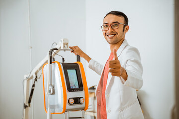 a handsome vet in doctor's coat smiling with thumb up while operating rontgen machine at petcare