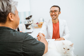 handsome vet in doctor's coat smiling while did a hand shake with the owner of the beautiful white cat