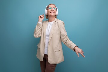 close-up portrait of a 50s middle-aged business woman in a jacket listening to music with headphones on a studio background with copy space