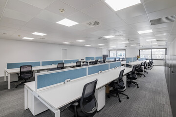An office in gray tones with long tables and chairs in a worker meeting room with large window and...