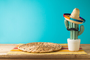 Empty wooden table with wicker place mat  and cactus decoration over blue wall  background. Mexican...