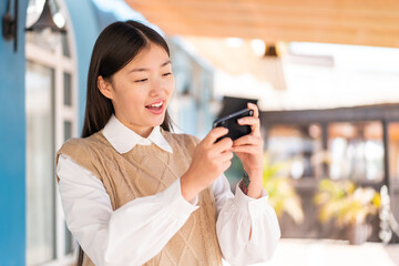 Fototapeta premium Young Chinese woman at outdoors playing with the mobile phone