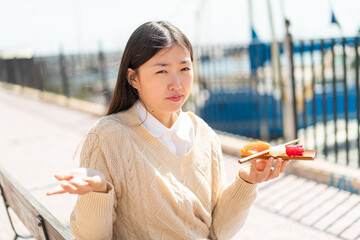 Young Chinese woman holding sashimi at outdoors making doubts gesture while lifting the shoulders