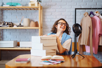 Young owner of an online store is recording live video on preparing parcels for shipping. Woman blogger talking with subscribers, recording video for vlog. Internet marketing and sales.