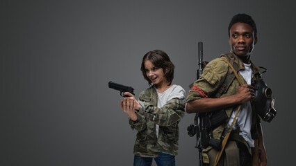 Shot of little girl with handgun and black man with rifle against grey background.