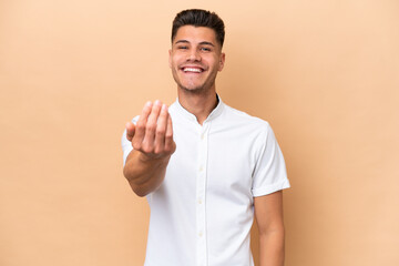 Young caucasian man isolated on beige background inviting to come with hand. Happy that you came