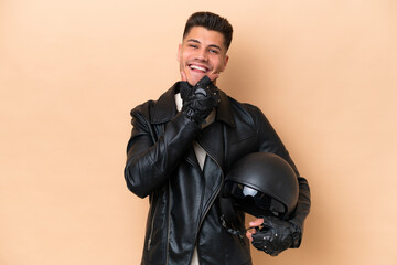 Fototapeta premium Young caucasian man with a motorcycle helmet isolated on beige background happy and smiling