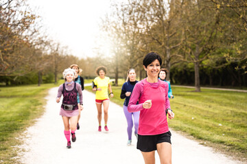 Multigenerational women running at the park - Group of female runners training outdoors for marathon race - Concept of wellness and body care in life course - Fit middle age woman in the foreground