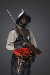 Shot of 18th century soldier with rifle dressed in armor against grey background.