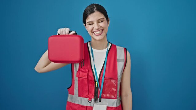 Young beautiful hispanic woman doctor smiling confident holding first aid kit box over isolated blue background