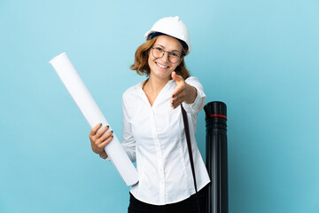 Young architect Georgian woman with helmet and holding blueprints over isolated background shaking hands for closing a good deal