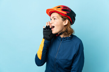 Young cyclist woman isolated on blue background shouting with mouth wide open to the side