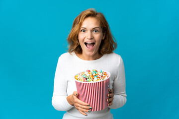 Young Georgian woman isolated on blue background holding a big bucket of popcorns