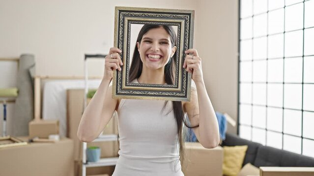 Young beautiful hispanic woman smiling confident holding frame at new home