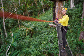 Young woman with climbing gear in an adventure extreme park climbing or passing on the rope road.