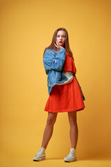 Summer urban fashion. Fun and colorful. Young pretty happy woman in orange dress posing against yellow background.