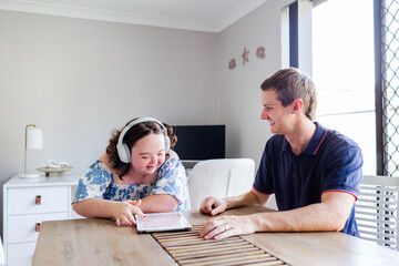 Teen wearing headphones talking with adult disability support worker in home office using tablet