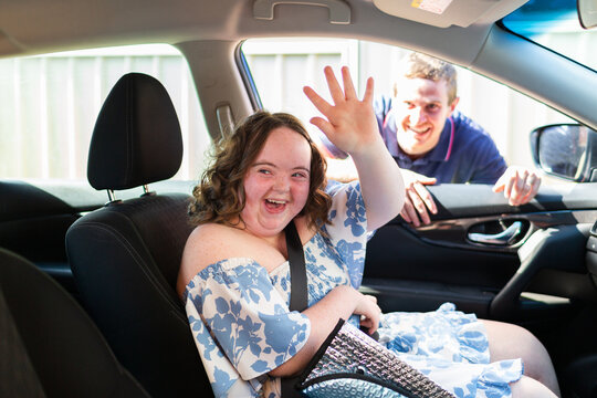 Happy young female person with down syndrome in car passenger seat waving goodbye