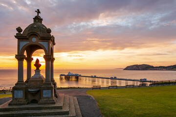 The Queen Victoria Monument overlooking the Llandudno Pier at sunrise in the seaside resort of Llandudno, North Wales.