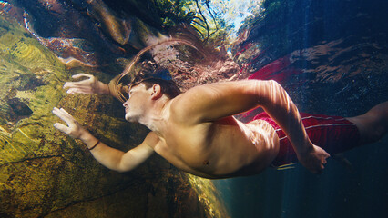 Man dives in the freshwater river with sunny rays shining through the water
