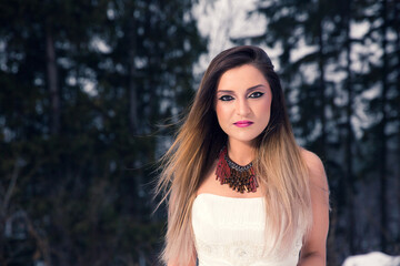 Portrait of pretty lady in wedding dress with long hair and bright makeup and jewelry on winter day